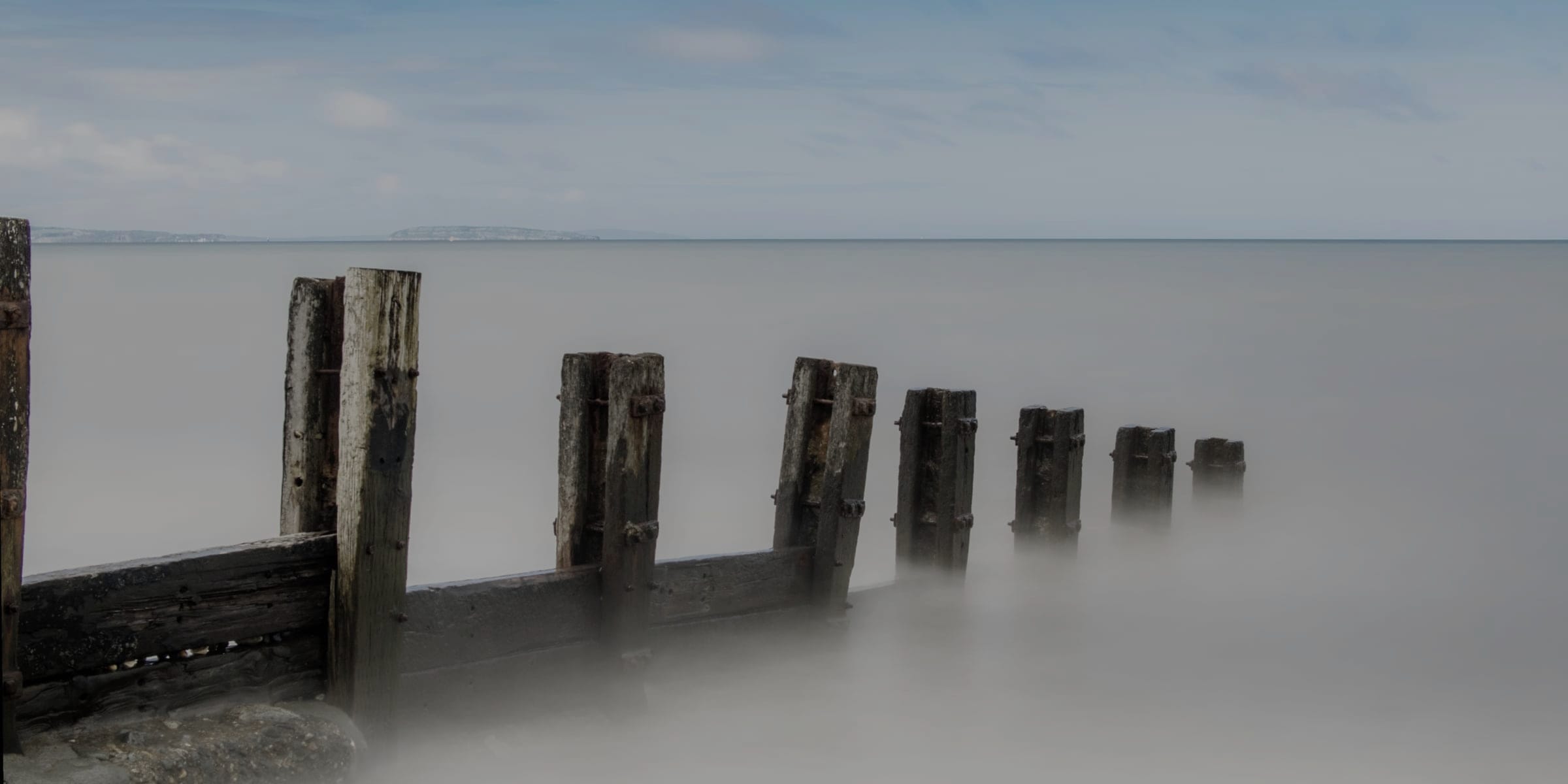 Mooring pilings standing in flat harbour water under an overcast sky.
